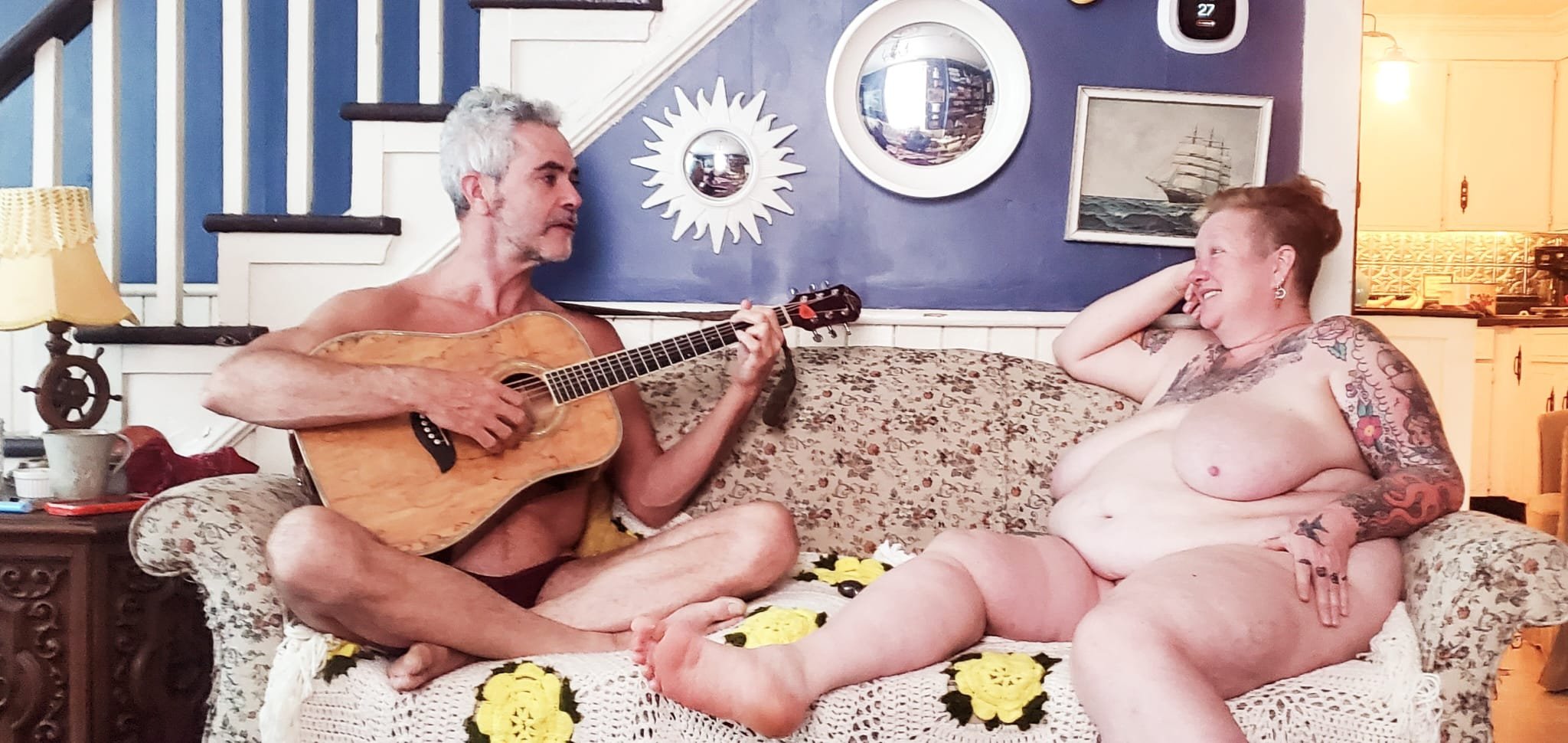 Brad playing guitar while Sara relaxes beside him in a comfortable home